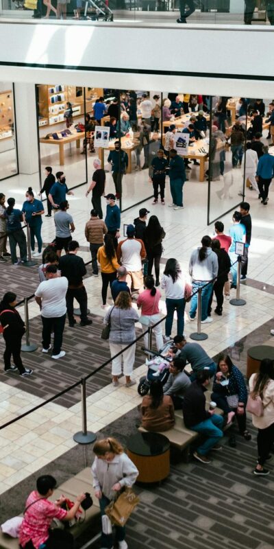 A bustling shopping center with a large crowd queuing inside an Apple Store.