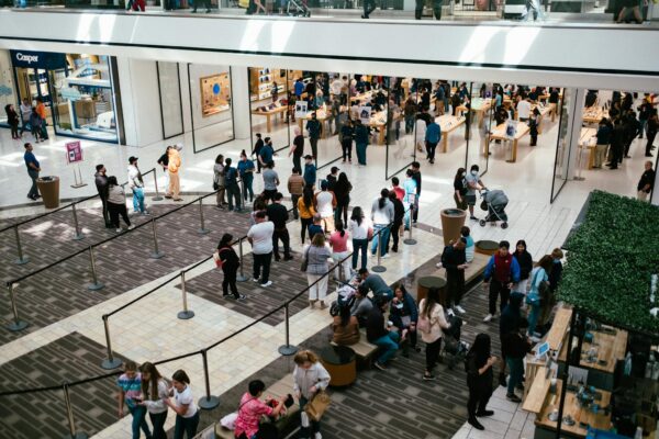 A bustling shopping center with a large crowd queuing inside an Apple Store.