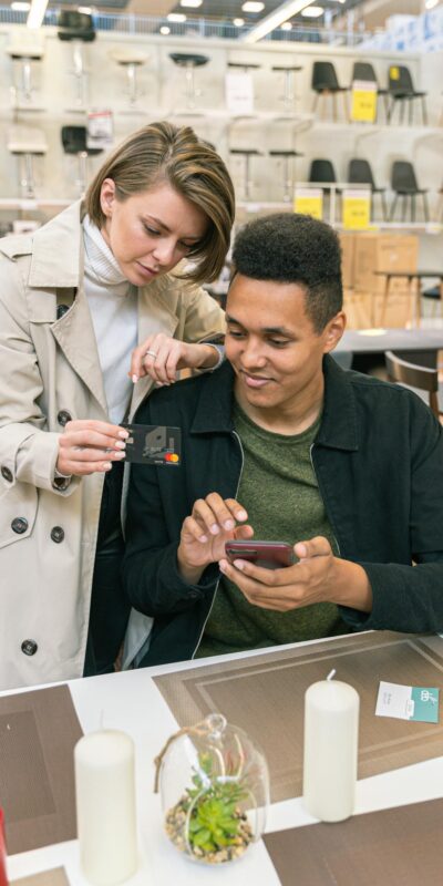 A couple makes a credit card payment using a smartphone in a modern furniture store.