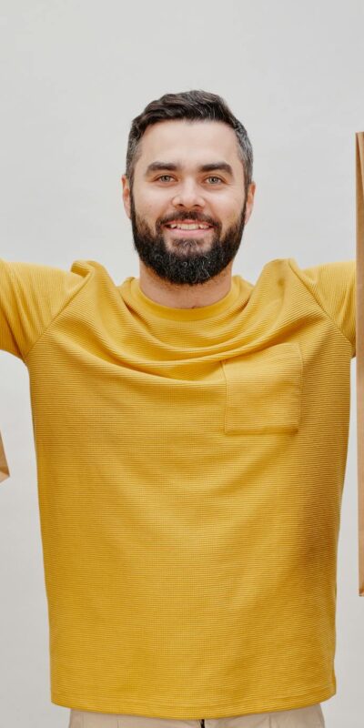 Happy man in yellow shirt holding multiple shopping bags, expressing joy of shopping.